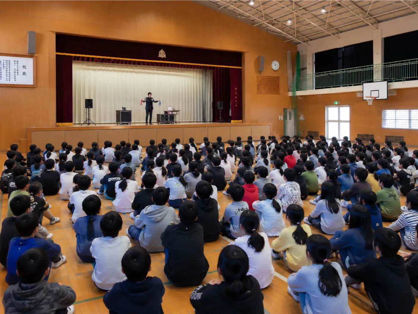 体育館のステージで大人数の子どもたちにマジックを披露する様子